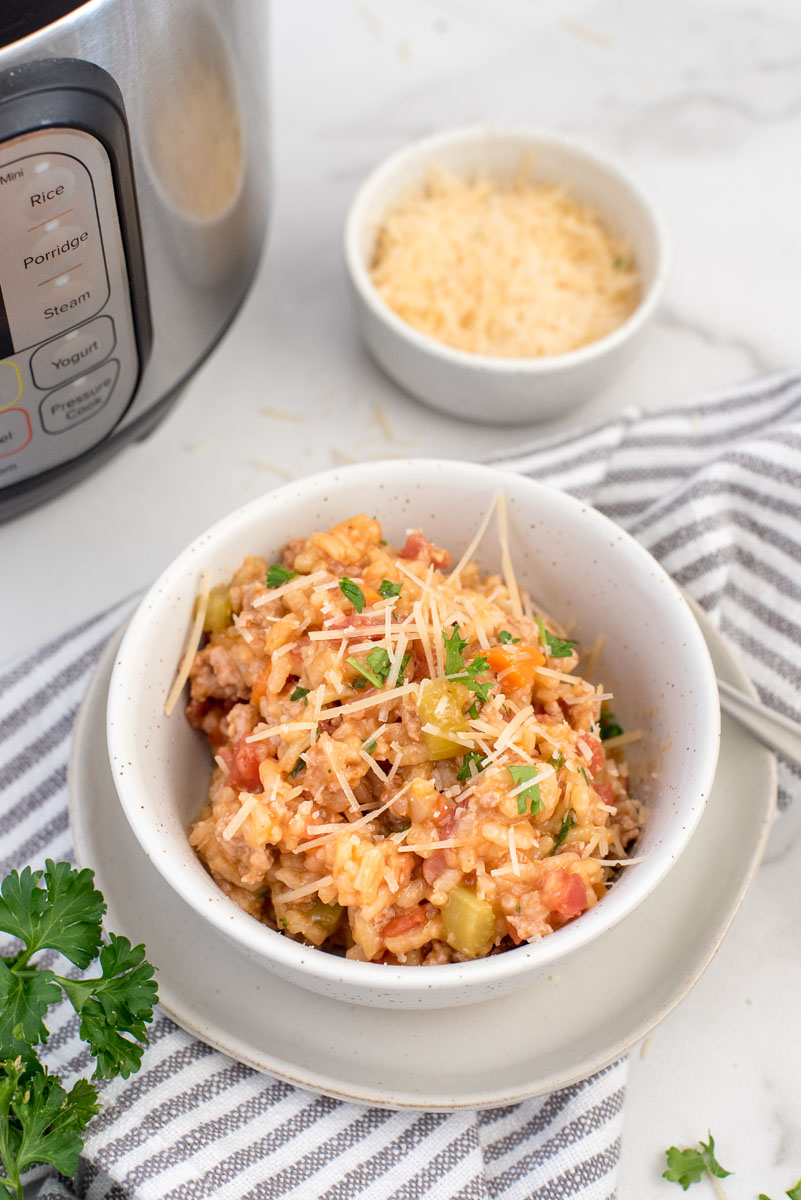Risotto Bolognese served in a bowl and topped with fresh parsley and grated parmesan on a gray and white napkin placed in front of an Instant Pot.