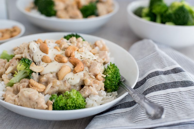 45 degree shot of rosemary cashew chicken served in a white bowl over rice and broccoli