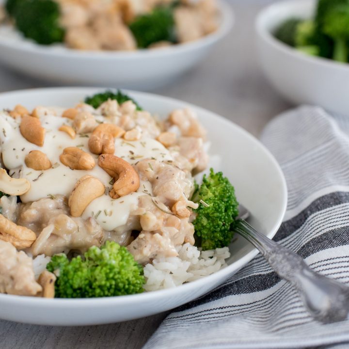 45 degree shot of rosemary cashew chicken served in a white bowl over rice and broccoli