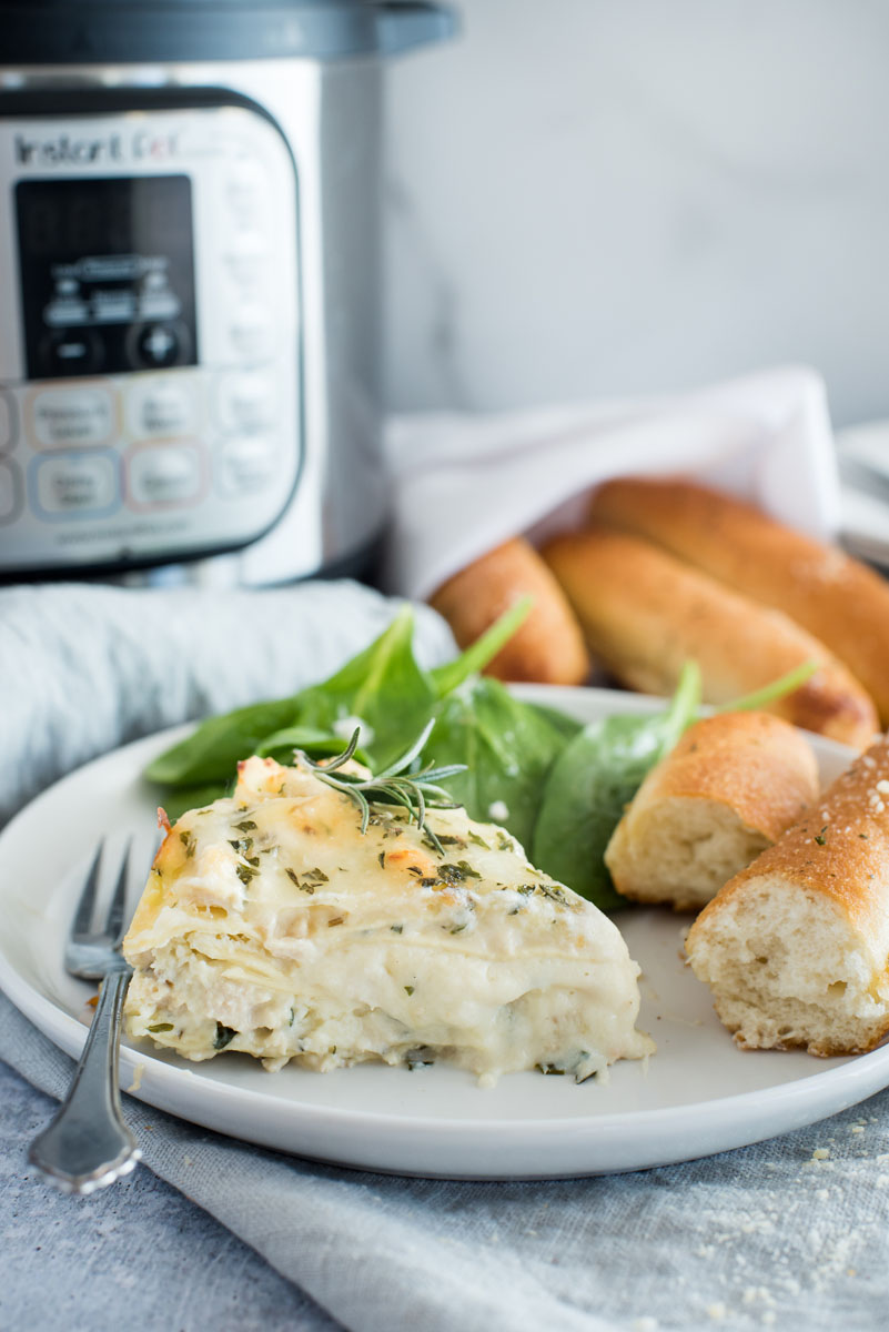 Instant pot white chicken lasagna on a white plate with a bread stick and greens