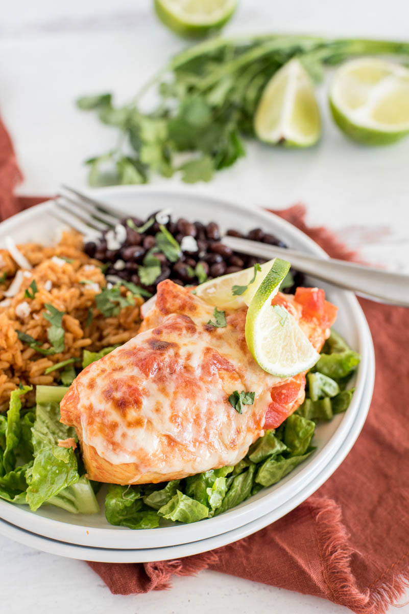 a 45 degree closeup vertical shot of Instant Pot Salsa Chicken, plated on a white plate and served on top of a bed of shredded lettuce, with a bunch of cilantro and additional limes in the background