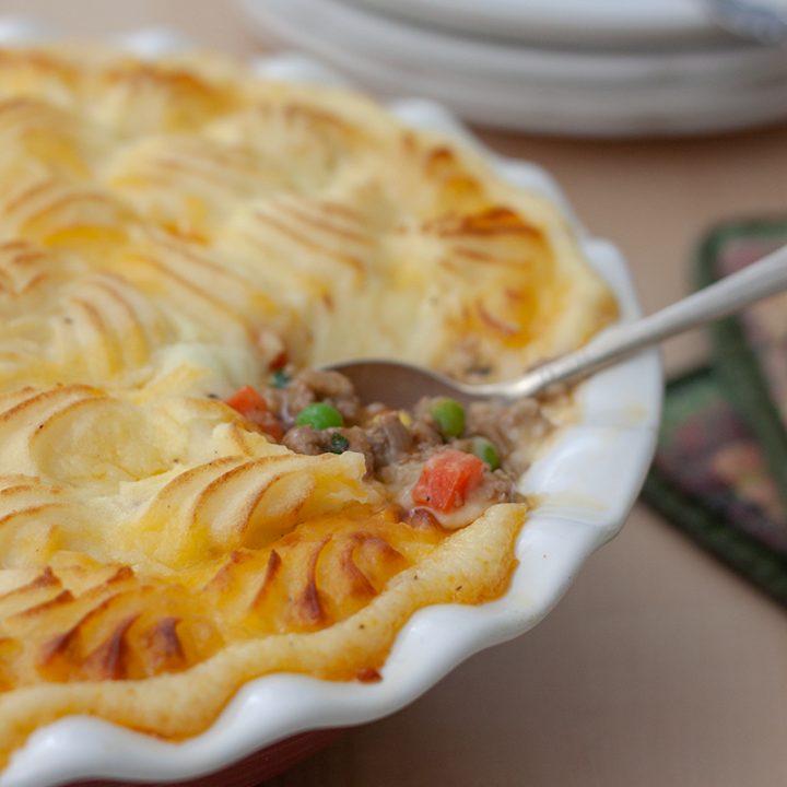 close shot of Instant Pot shepherds pie topped with mashed potatoes and browned in the oven, with a silver spoon showin gthe ground beef, carrot, and corn filling.