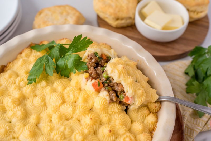 Dishing up Instant Pot shepherds pie from a serving dish garnished with parsley.