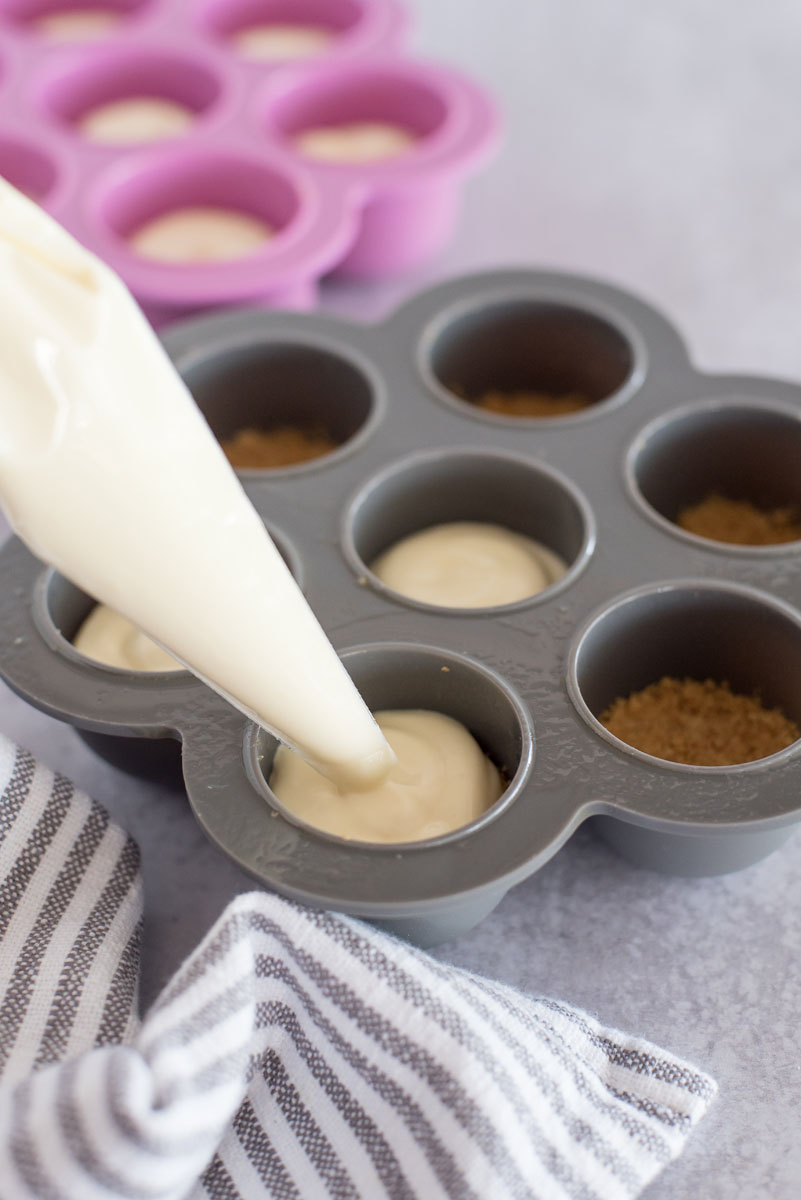 filling a silicone egg bite mold with a piping bag full of cheesecake filling 