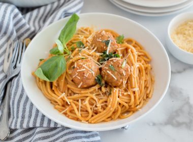 Close up of white bowl with spaghetti and meatballs, spaghetti sauce and fresh basil leaves