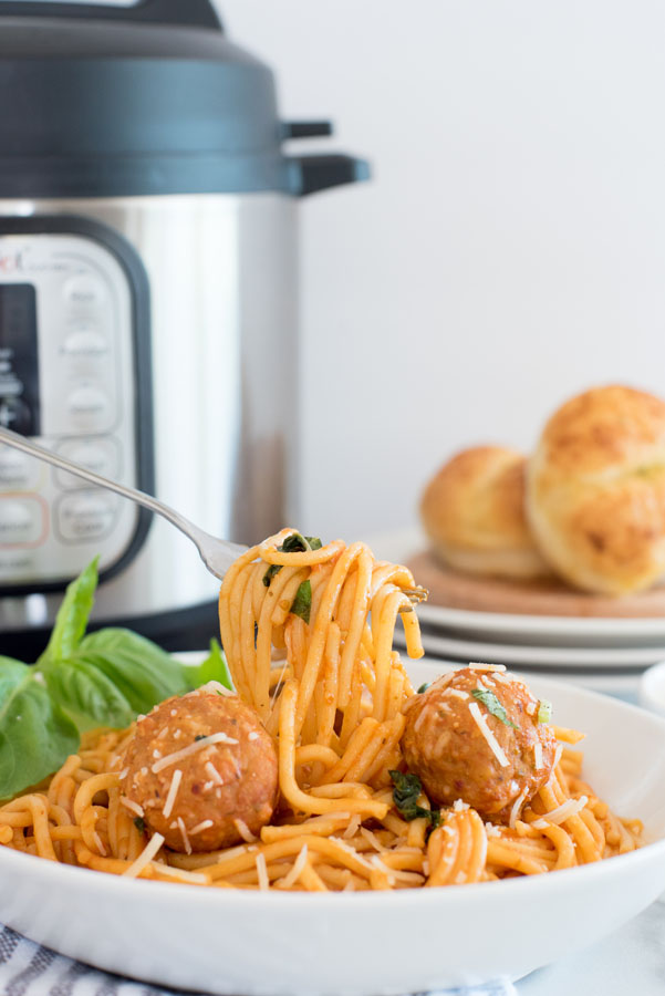Instant pot spaghetti and meatballs with a bite being taken out with a fork in front of an instant pot electric pressure cooker