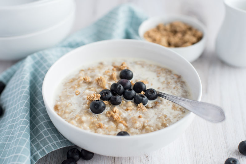 pressure cooker steel cut oats with fresh blueberries in a white cereal bowl with a teal checkered napkin