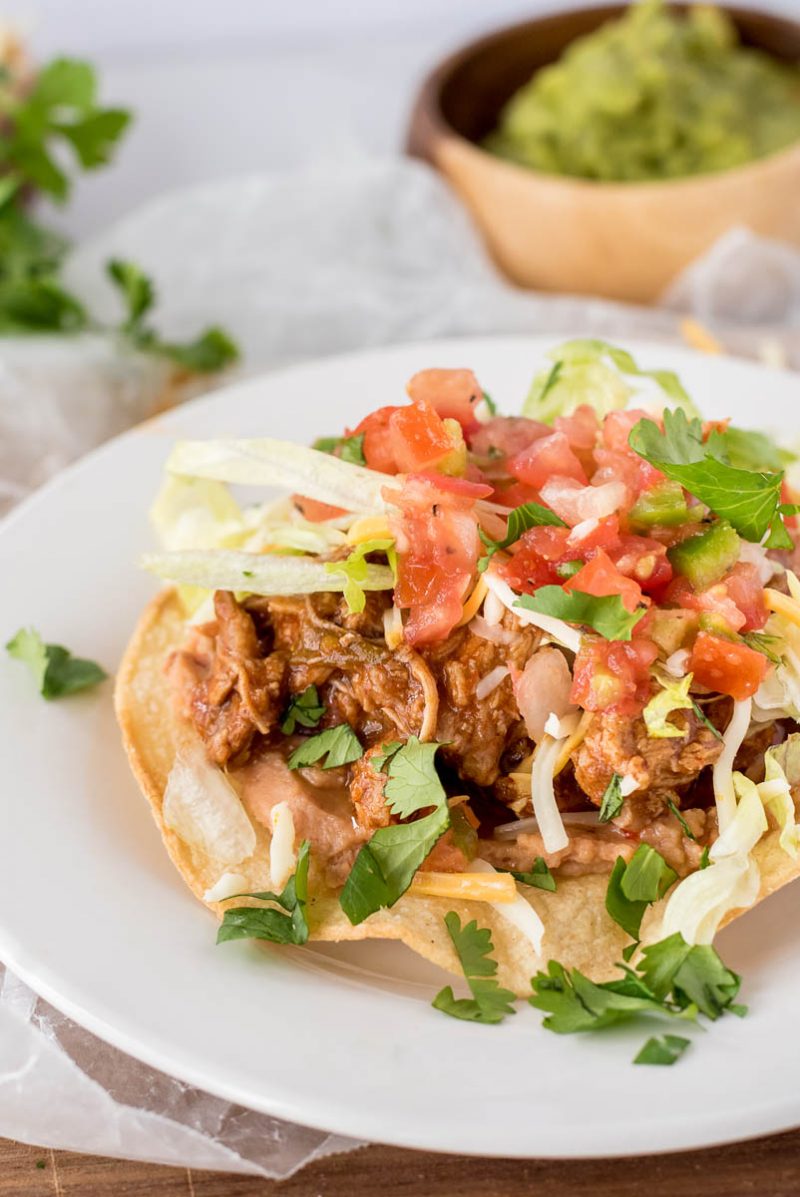 close  up on a tostada topped with sweet pork, tomtatoes and fresh herbs