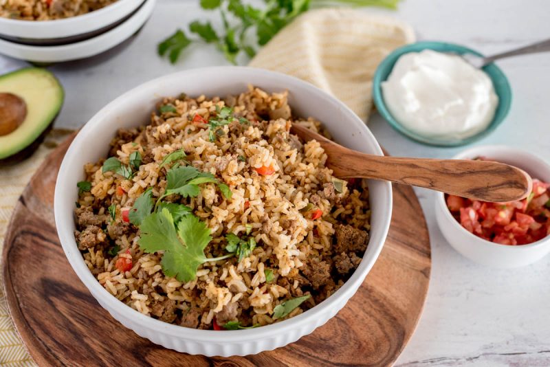 white bowl with instant pot taco rice and sour cream and tomatoes on the side