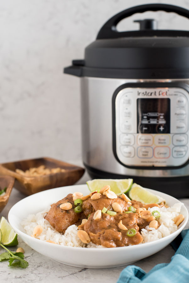 Instant pot/pressure cooker thai chicken thighs with peanut sauce and white rice in front of an elelctric pressure cooker