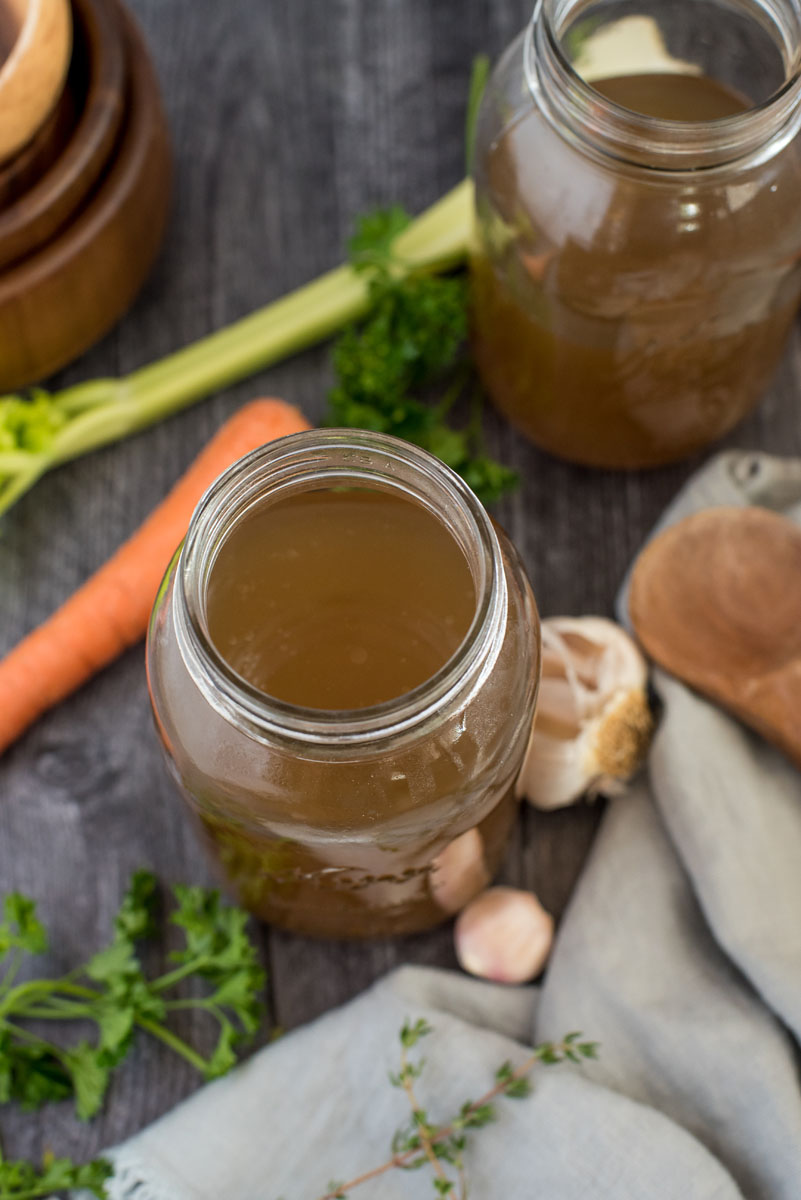 Overhead shot of Instant Pot turkey stock in a mason jar surrounded by a wooden spoon, fresh parsley, carrots, and cellery