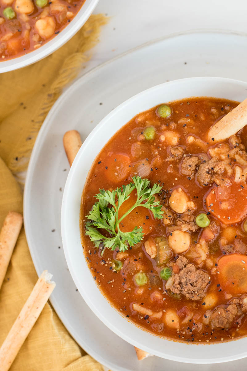 Overhead, close up shot of Instant Pot vegetable beef soup garnished with a fresh sprig of parsley and served in a white bowl.