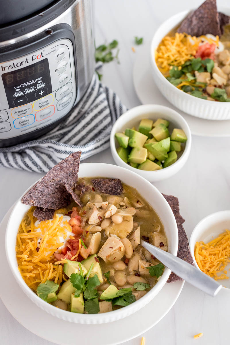 bowl of instant pot white chicken chili with avocado, chips and shredded cheese on top