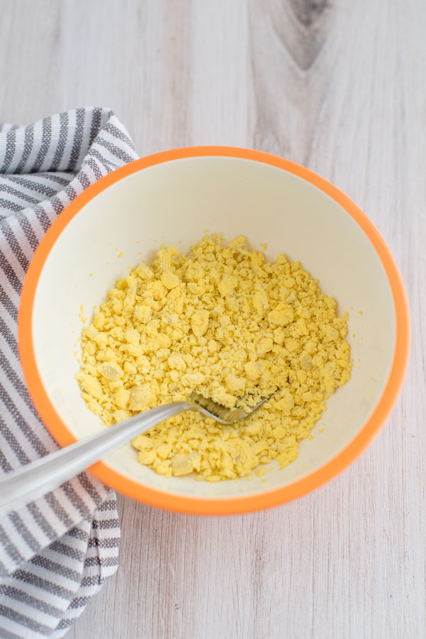 Close up on a white bowl with hard-boiled egg yolks being mashed with a silver fork