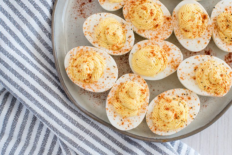 Overhead of a ceramic plate with 10 half hard-boiled eggs made in an electric pressure cooker filled with deviled egg yolk filling 