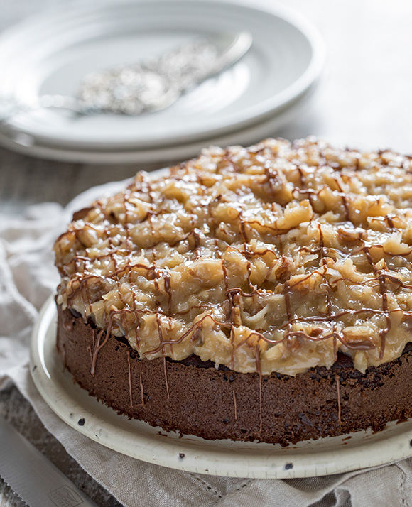 45 degree shot included in the Instantly Sweet Dessert Cookbook - featuring a white plate topped with german chocolate cake with coconut almond frosting and a crisscross chocolate drizzle