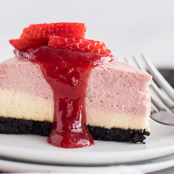 Close up of a layered strawberry cheesecake, cooked in an Instant Pot pressure cooker, garnished with a drizzle of strawberry sauce and fresh strawberries