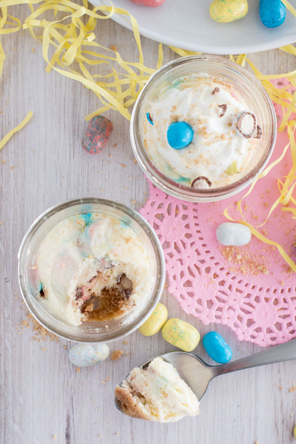 Overhead of a mini Robin Egg Cheesecake made in a pressure cooker on a white wooden table decorated for Easter with one bite taken out on a metal spoon nearby.