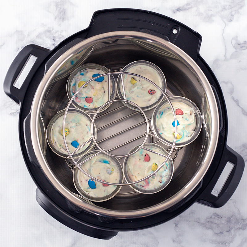 Six Instant Pot mini cheesecakes in the bottom of the pressure cooking pot, with a second trivet stacked on top