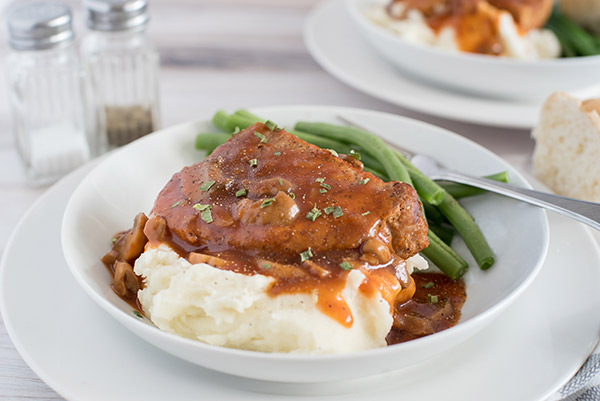 pork and gravy served on a white plate with  green beans 