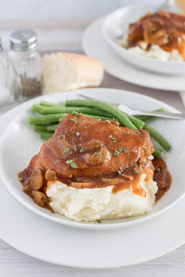 Plated boneless pork chop and gravy over mashed potatoes with green beans on the side