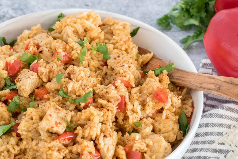 Close-up of the Instant Pot spanish style chicken and rice with a wooden spoon, cilantro, and bell peppers in the background