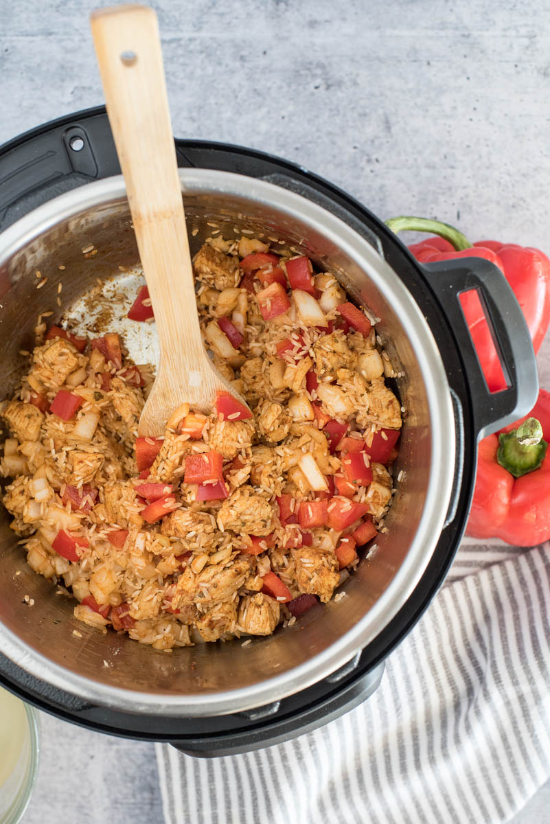 An overhead shot looking into an Instant Pot filled with Spanish-style Chicken and Rice, with a wooden spoon in the top left of the frame