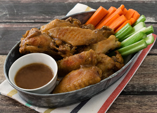 Instant Pot Teriyaki Chicken wings, ready to serve in a tin with carrots and celery and extra dipping teriyaki sauce