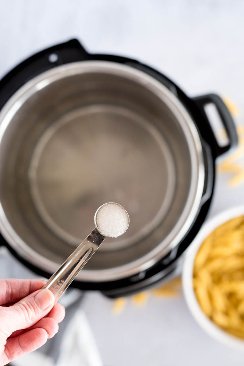 Overhead shot of adding salt to the water for making Instant Pot Pasta 