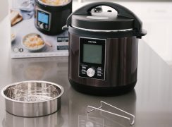 The Zavor LUX pressure cooker placed on a counter with the included trivet and steamer basket placed in front of the packaging box.