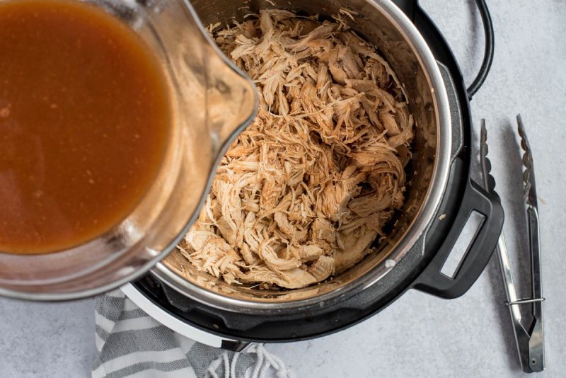 an overhead shot of the liquids being poured back into the shredded chicken inside of the Instant Pot