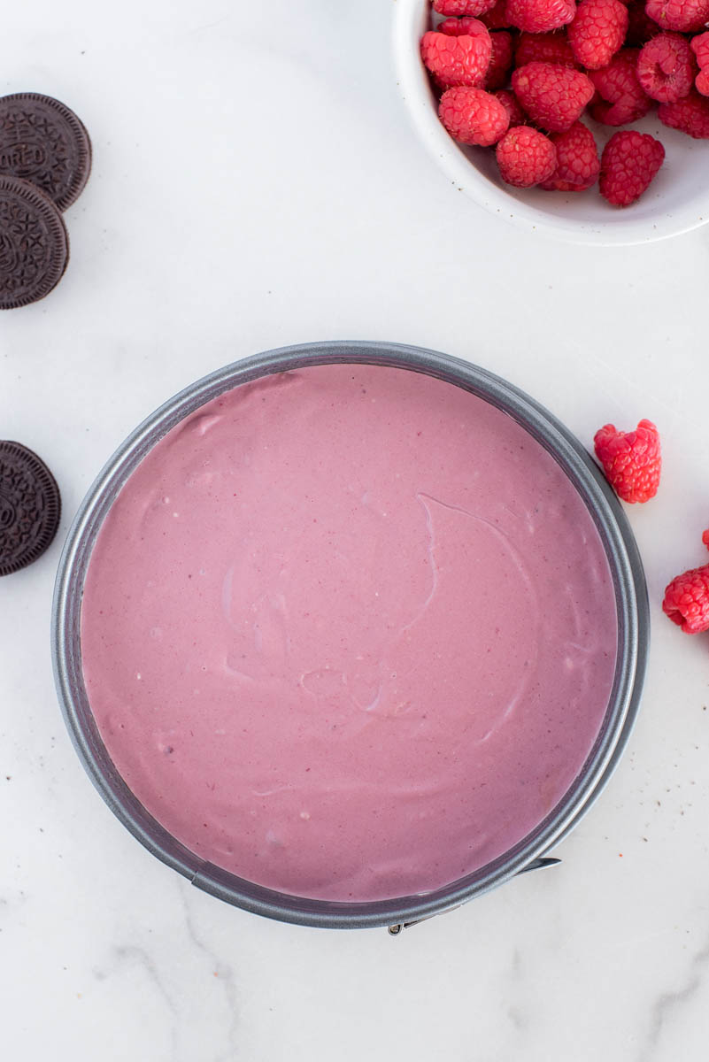 an overhead shot of the cheesecake with the batter poured into the silicone pan, with oreos and fresh raspberries in the background