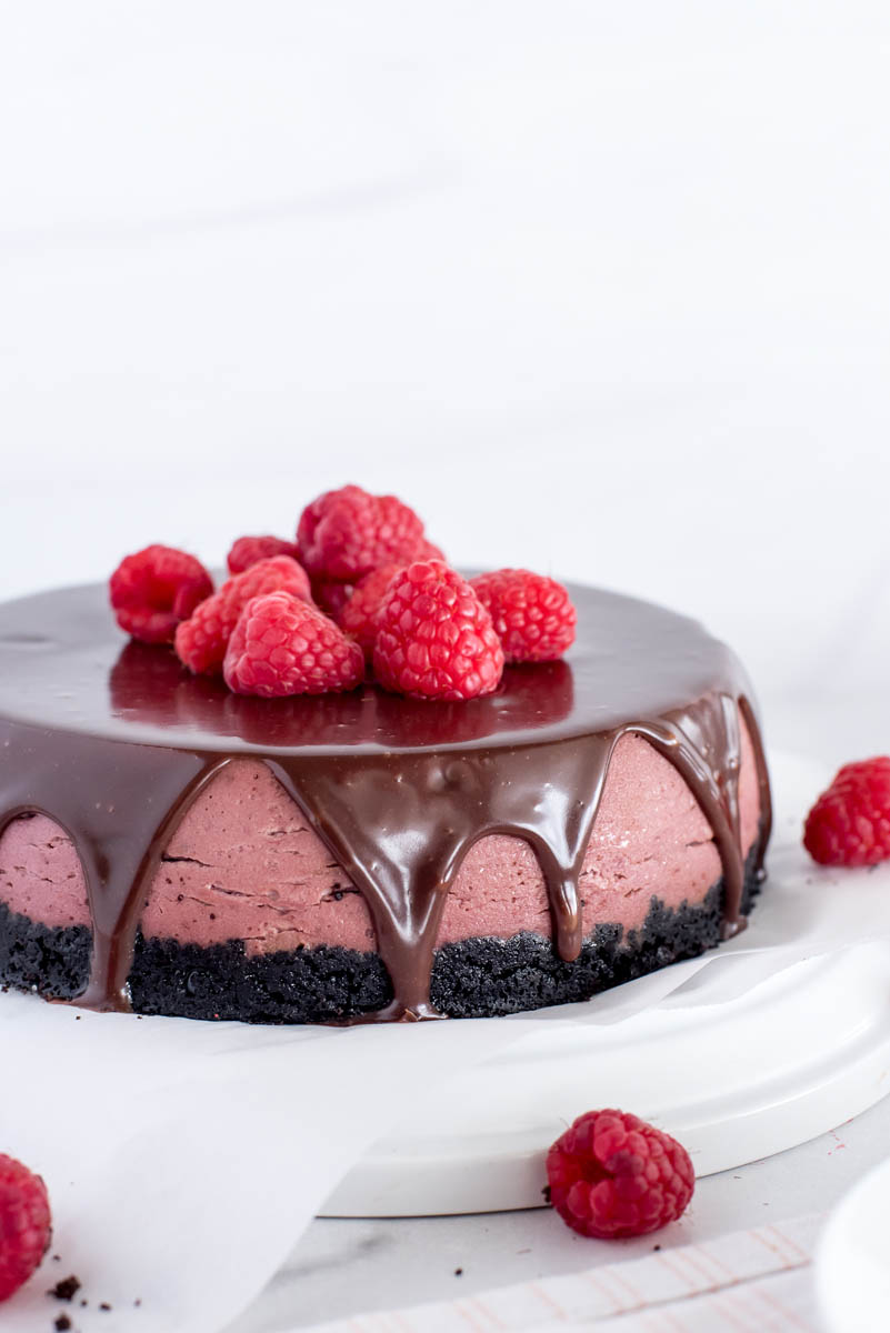 A close-up side shot of the finished raspberry cheesecake, covered in chocolate ganache with fresh raspberries on top.