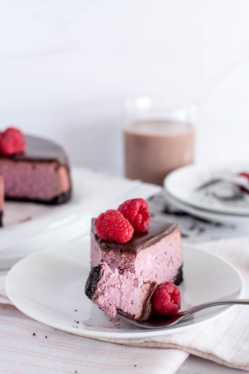 a fork with a bite of raspberry cheesecake and a fresh raspberry on it
