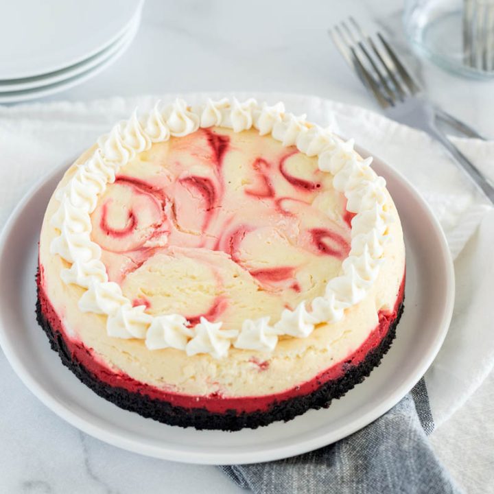 An overhead shot of the red velvet cheesecake on a white plate, with small whipped cream swirls at the sides.