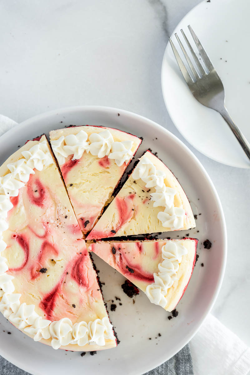 An overhead shot that clearly shows the red swirls in the red velvet cheesecake, with one slice missing and three others cut before serving