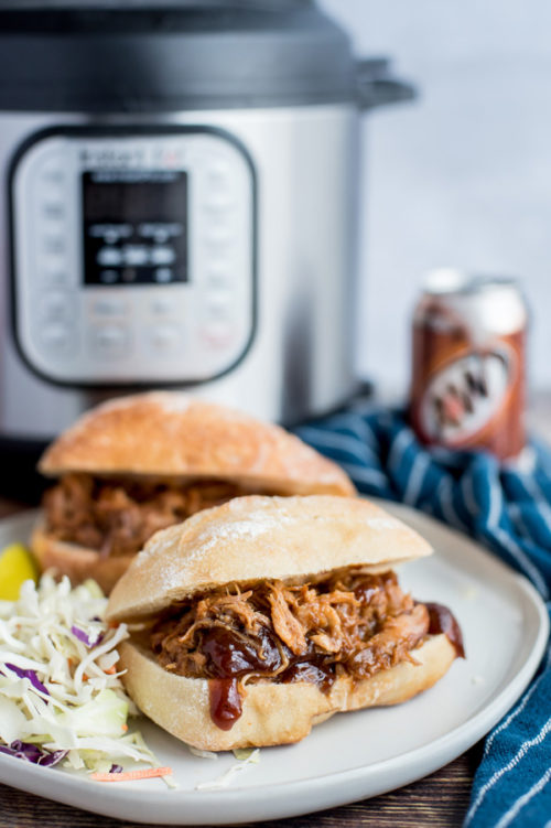 Pressure Cooker Root Beer Pulled Pork sandwiches plated and ready to serve with an Instant Pot in the background