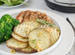 a close-up shot of the rosemary new potatoes garnished with salt, garlic, and rosemary, on a plate iwth broccoli and grilled chicken faded into the background