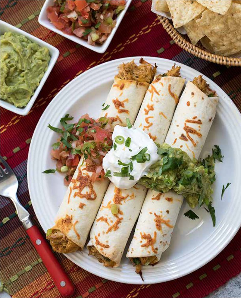 Baked Chicken Taquitos from the Electric Pressure Cooker Cookbook - featuring overhead shot of a white plate with three taquitos on top, garnished with tomato salas, guacamole, sour cream, cilantro and green onions