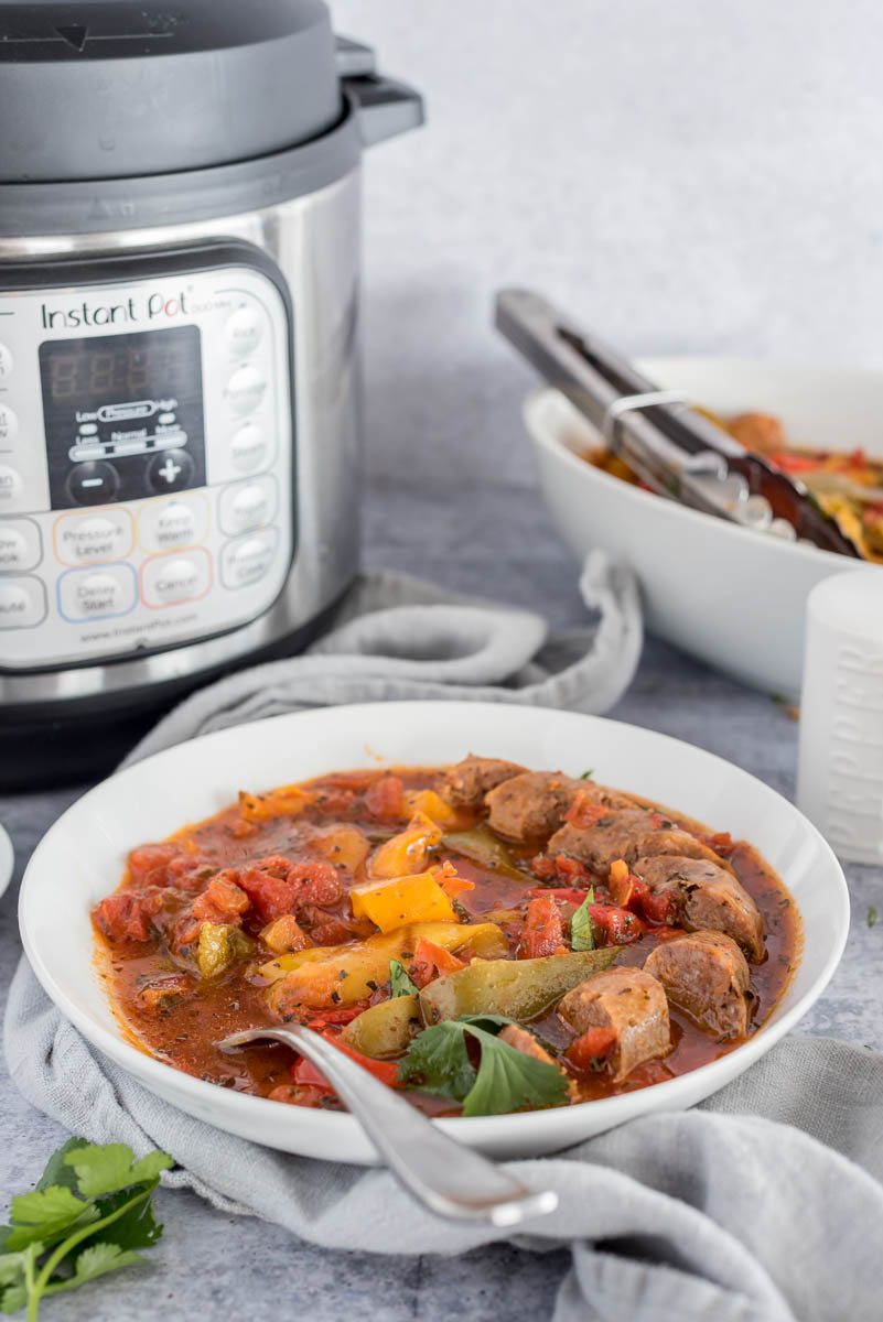 Pressure cooker sausage and peppers in a white bowl over a gray napkin, and placed in front of an Instant Pot.