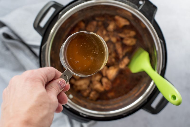 Overhead of an Instant Pot filled with pressure cooked Honey Sesame Chicken with honey being added from a metal liquid measuring cup to make a sauce.