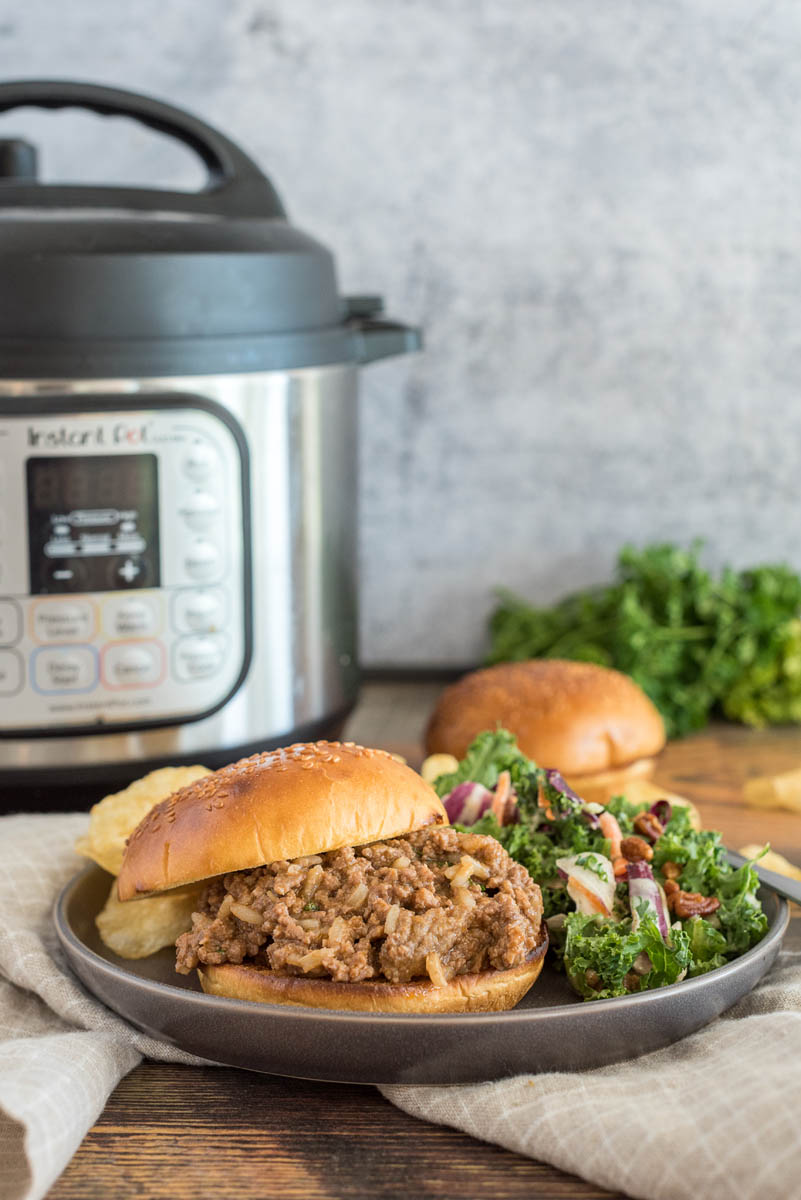 Quick sloppy joes made with frozen beef, served on a bun with salad and potato chips, and placed in front of an Instant Pot.