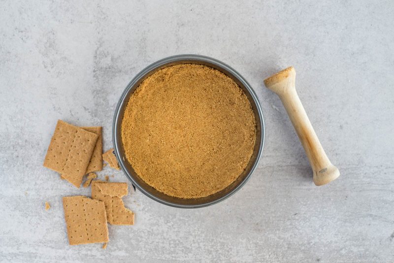 Graham cracker crust in a spring form pan with a tamper, for s'mores cheesecake.