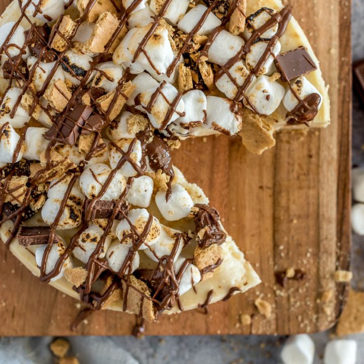 Overhead picture of an Instant Pot s'more cheesecake topped with marshmallows, graham crackers, and chocolate, placed on a wooden cutting board.