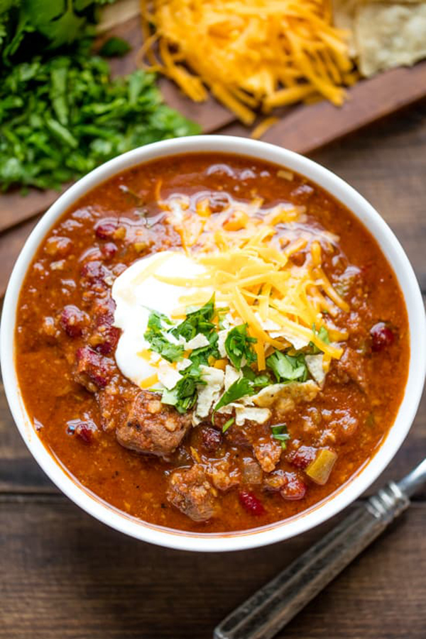 overhead shot of Instant Pot Chili from the Stay at Home Chef's review of the Electric Pressure Cooker Cookbook - featuring a white bowl on a dark wooden background, filled with red cili, topped with sour cream, cheese, and cilantro garnish