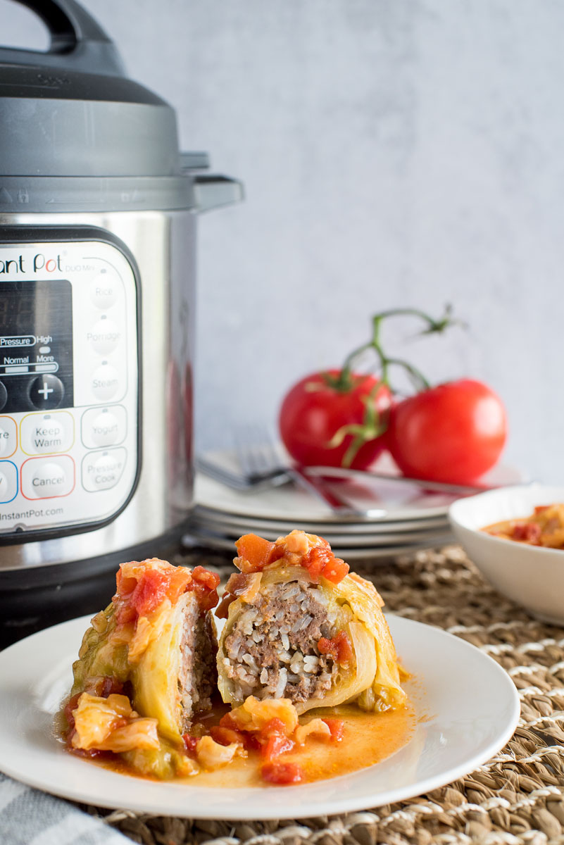 one stuffed cabbage roll cut in half on a plate with an instant pot in the background