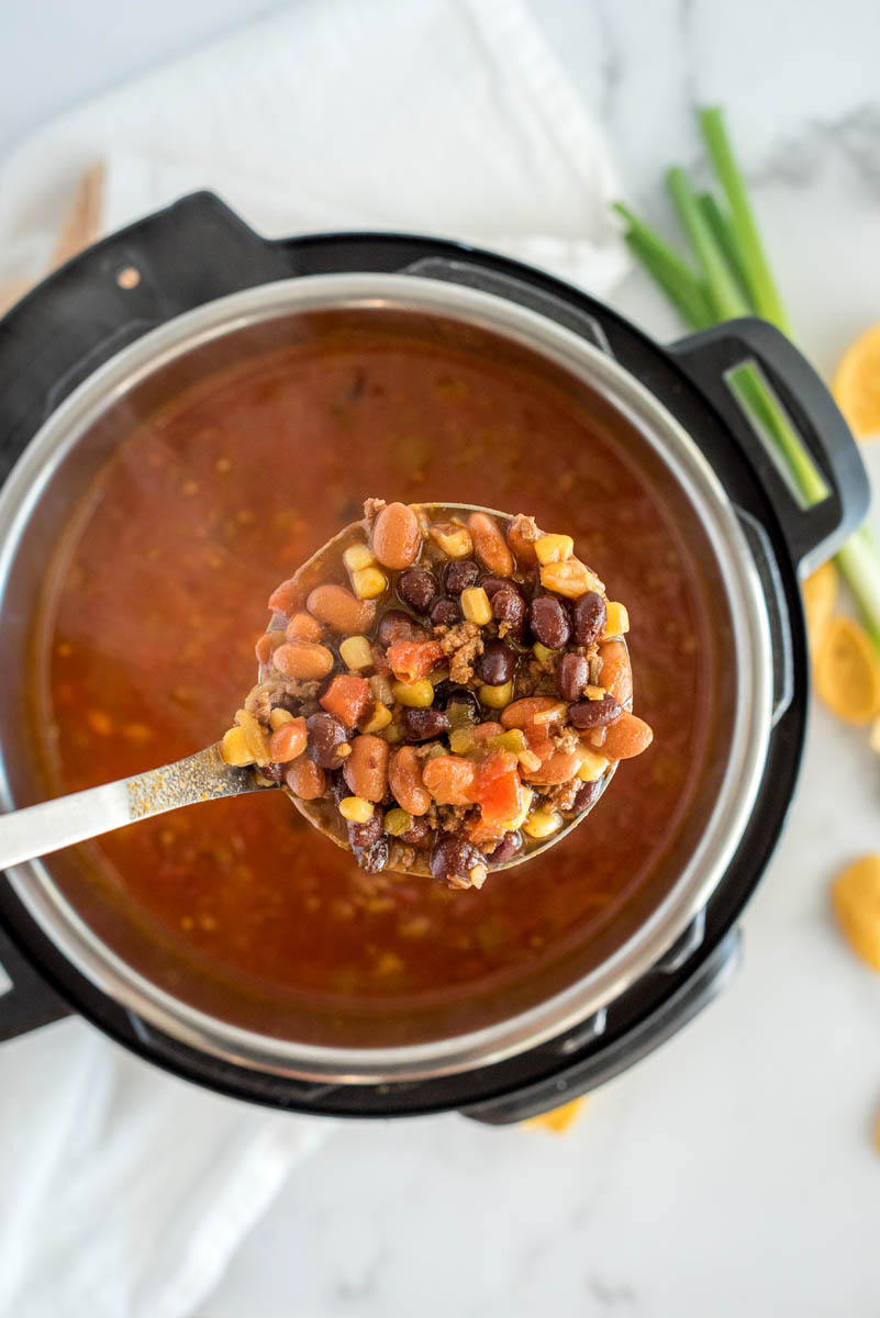 Overhead picture of an Instant Pot with taco soup cooked inside and a spoonful of diced tomatoes, beans, corn, and meat over the top.