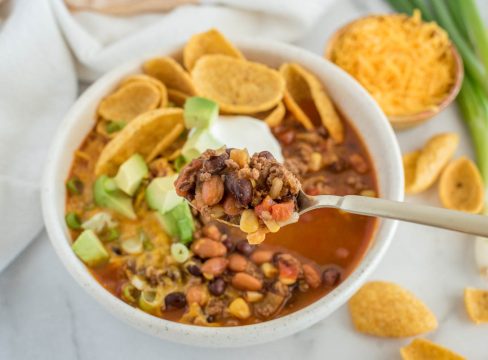 A close up picture of a spoonful of Instant Pot taco soup on a spoon, over a bowl of soup topped with sour cream, avocado, and chips.