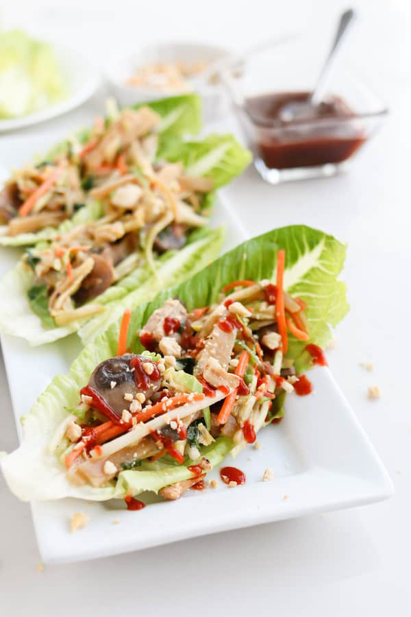 45 degree shot of Instant Pot Moo Shu Pork from Tidbits' review of the Electric Pressure Cooker Cookbook - featuring a white platter with three long lettuce leaves filled with moo shoo pork and garnished with matchstick carrots and red sauce