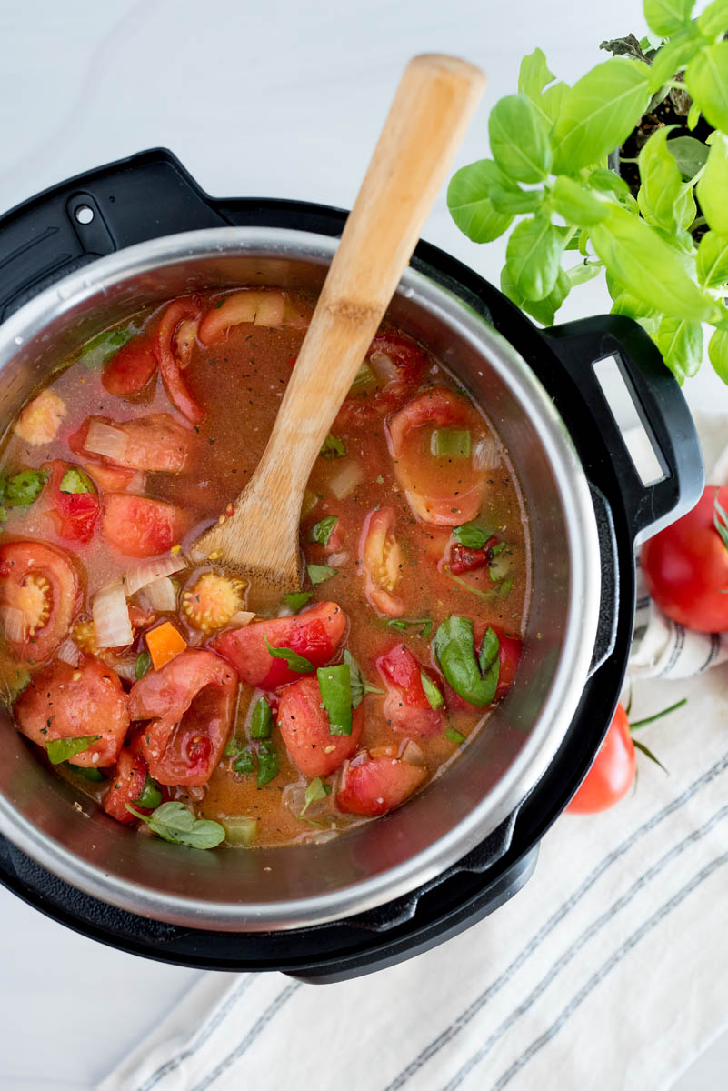 an overhead shot looking into an Instant Pot filled with fresh garden tomatoes, broth, and basil, ready to pressure cook